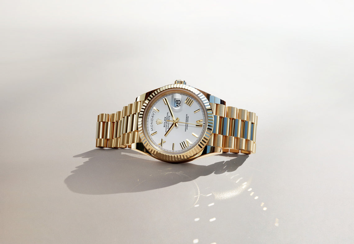 The 18K yellow gold Rolex Day-Date 40 lying on its side, crown up. This watch has a 40mm case and is made from solid gold. The dial on this watch is white with Roman numerals and has a fluted bezel. Model #228238.