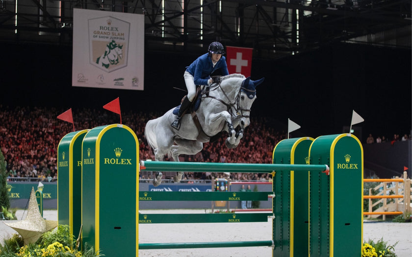 A horse mid-air leaping over Rolex-branded log fences at a tournament.