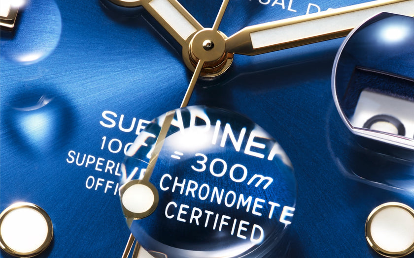 A close up of the royal blue dial on the Rolex Submariner 18K yellow gold and Oystersteel version. There is a drop of water on the sapphire crystal magnifying the 300M waterproofness description on the dial. Model #126613LB.