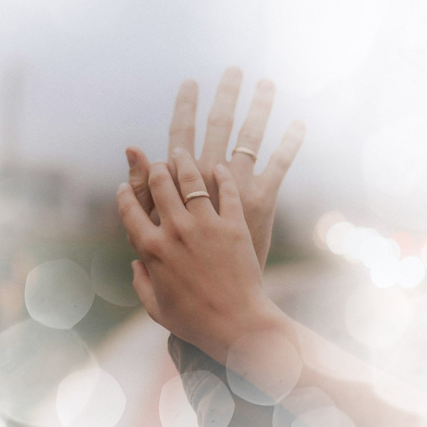 A groom sliding a wedding ring onto his bride's hand, on a teal background.