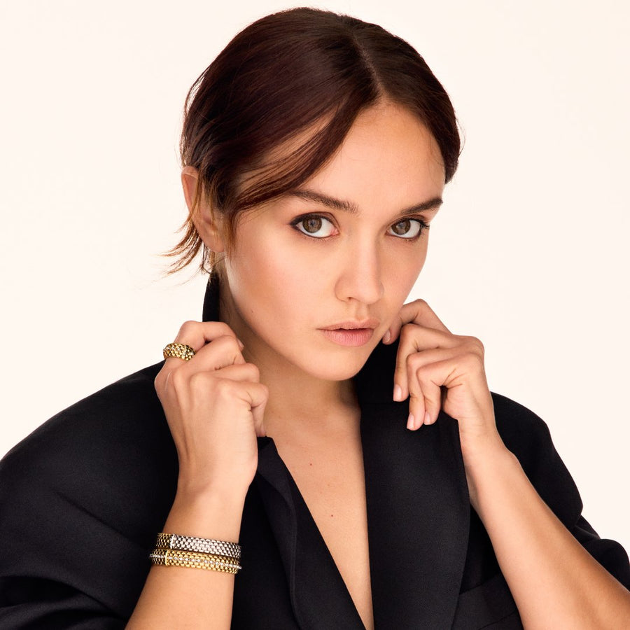 A fashionable woman reading a book and drinking coffee while wearing FOPE bracelets.