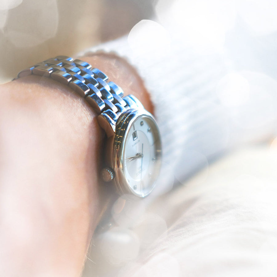 A classic watch on leather lying on its side with a teal background.