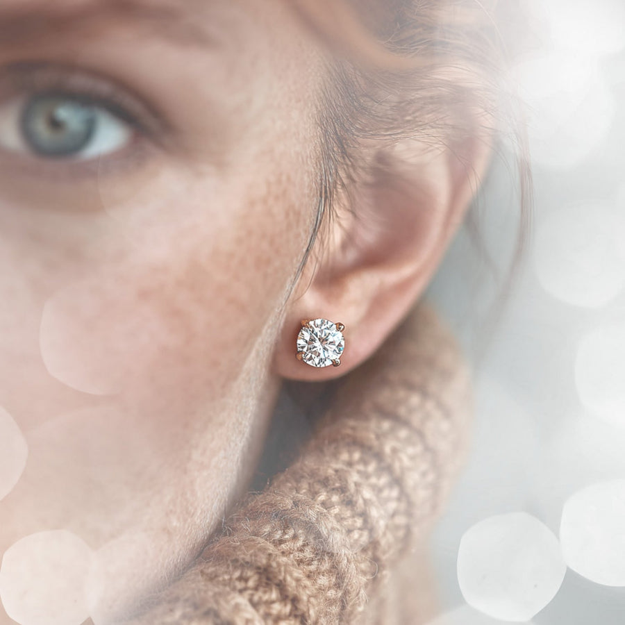 Close up of a diamond halo stud earring on an ear with a teal background.