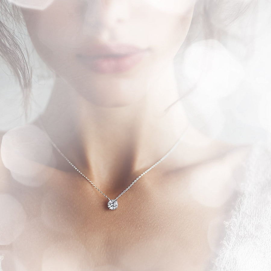 A woman with her head turn showing off a stunning diamond necklace with a teal background.