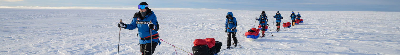 A group expedition snowshoeing on ice and snow while pulling their equipment.
