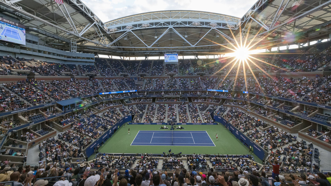 The US Open of Tennis at Flushing Meadows in a full stadium with the sun shining through the rafters.