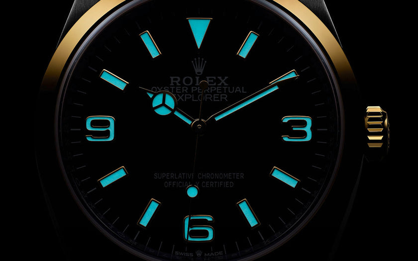 A close up of the dial of the Rolex Explorer in 18K yellow gold and Oystersteel. The dial is glowing in the dark, displaying the new Chromalight display exclusive to Rolex. The hands, indices, and 3, 6, 9 Arabic numerals are glowing.