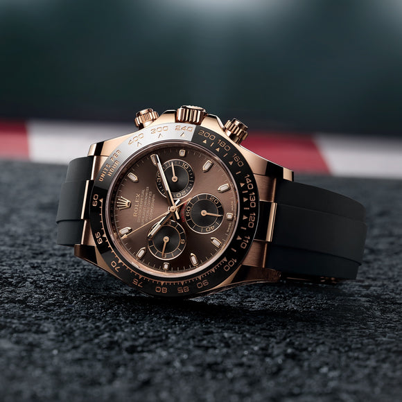 The Rolex Cosmograph Daytona in 18K Everose gold, lying on its side with the crown and pushers pointing up. The watch features a black ceramic dial with tachymetre scale, chocolate dial, and an Oysterflex bracelet. Model #116515LN.