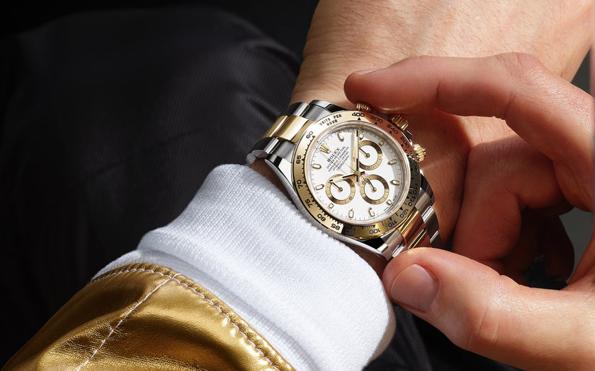 The Rolex Cosmograph Daytona on the wrist of a driver. The person is using the stop/start feature of the chronograph function. The watch has a white dial and is made in Oystersteel and 18K yellow gold. Model #116503.