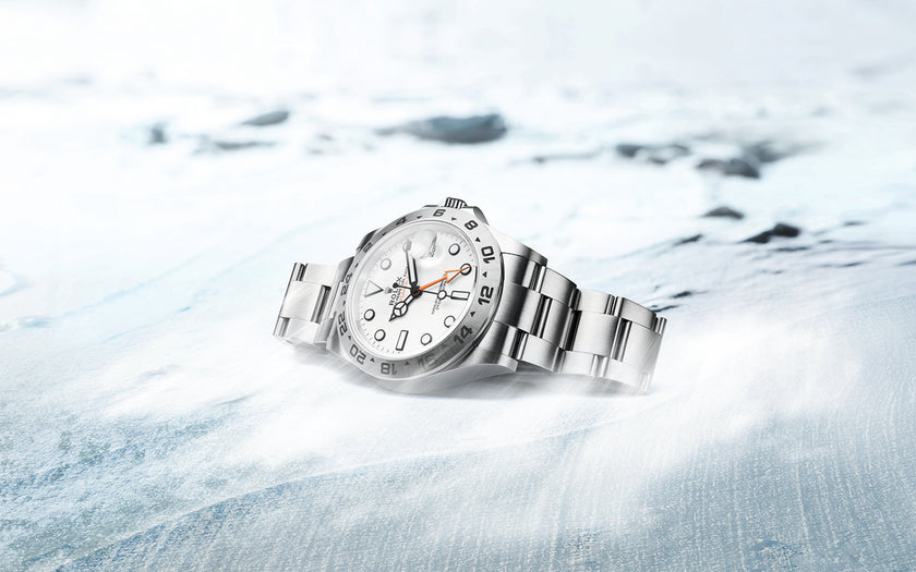 The Rolex Explorer II in Oystersteel with a white dial. The watch is lying on a piece of ice, crown up, with mist surrounding it. Model #226570.