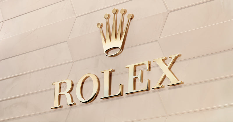 The Rolex logo in gold on a wall.