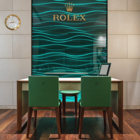 Our Rolex sales desk featuring two green leather chair, and a green wavy Rolex back wall lit from underneath.