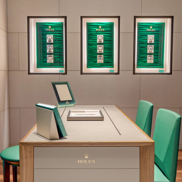 A side view shot of our selling desk with our 3 Rolex displays in the background. The desk has a green leather stool on the left side and 2 green leather chairs on the right.