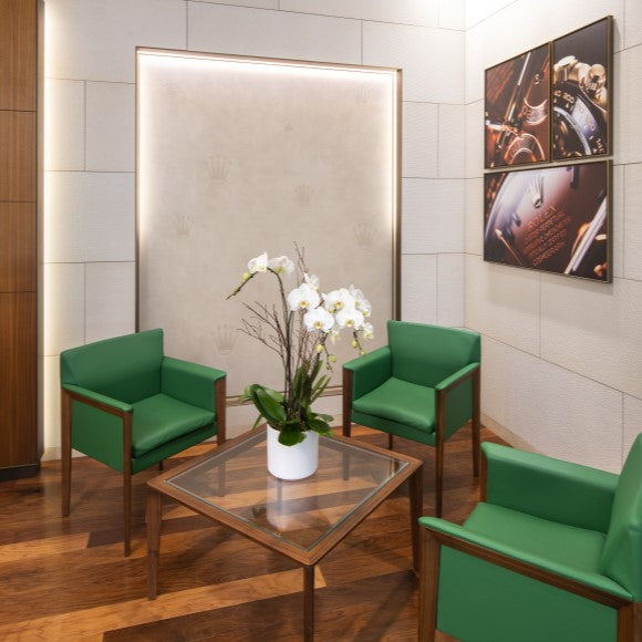 Our Rolex sitting area featuring three green leather chairs and a glass table with white orchids.